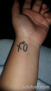 Фото тату: надпись 'xo' с маленьким сердечком, выполненная черными чернилами на запястье. Минималистичный и романтичный дизайн.