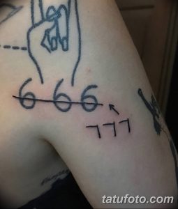 Фото тату на плече с изображением числа 666 и руки, показывающей знак 'козлиной головы'. Черный контурный рисунок татуировки.