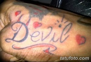 Фото татуировки надписи 'Devil' с изображением сердечек на стопе. Цветной рисунок татуировки в стиле олдскул, выполненный яркими красками.