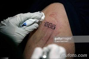 Фото тату: процесс нанесения татуировки с числом "666" на плече мужчины, мастер в перчатках. Реалистичное изображение процесса татуировки.