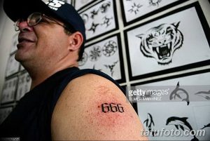 Фото тату: татуировка с числом "666" на плече мужчины, на фоне эскизов татуировок. Простой и провокационный рисунок татуировки.