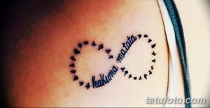 Фото тату: черная татуировка с надписью 'Hakuna Matata' в форме символа бесконечности, украшенного птицами. Яркий и позитивный дизайн.