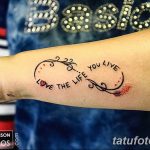 Фото тату: надпись "Love the life you live" в виде спирали на запястье, украшенная небольшими сердечками и капельками крови. Красивый и мотивирующий рисунок татуировки.