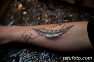 Фото тату пера и надписи 'life is love' на запястье. Черно-серый рисунок татуировки выполнен в реалистичном стиле с детальной прорисовкой пера.