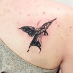 Фото тату ласточки на ключице. Черно-красный рисунок татуировки с детально проработанными перьями и брызгами краски. Идея для тату для девушек.