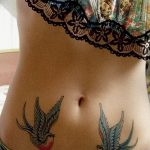 Фото тату двух ласточек на животе. Цветная татуировка в стиле олд скул с яркими синими, красными и черными цветами. Детализированный рисунок с четкими контурами.