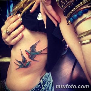 Фото тату двух ласточек на боку девушки. Цветной рисунок татуировки с детально проработанными крыльями и ярким оперением.