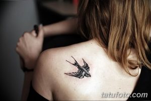 Фото небольшой татуировки ласточки на лопатке. Рисунок выполнен в черно-серых тонах с использованием тонких линий.