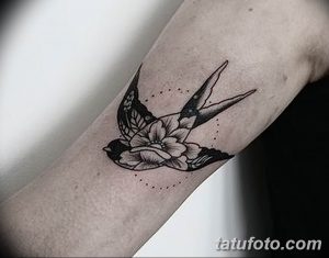 Фото тату ласточки с цветами на руке, выполненной в технике blackwork с точками. Детализированный рисунок татуировки.