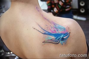 Фотография акварельной татуировки ласточки на плече. Мягкие переходы цветов и нежный дизайн.