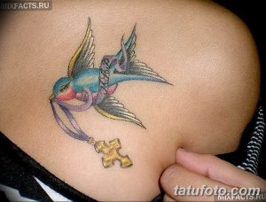 Фото татуировки ласточки с ключом и крестом на ключице. Цветная татуировка выполнена в традиционном стиле.