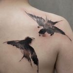 Фото акварельной татуировки двух ласточек на груди. Черно-серая татуировка с размытыми краями, создающая эффект акварельного рисунка.