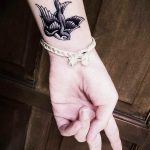 Фотография татуировки ласточки на запястье девушки. Татуировка выполнена в черно-белой гамме, с детальной проработкой перьев и изящной линией контура.