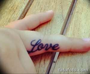 Фото минималистичной татуировки с надписью 'Love', выполненной черными чернилами на пальце руки.