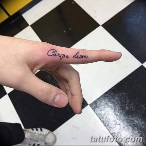 Фото тату: надпись "Carpe diem" на пальце руки, выполненная каллиграфическим шрифтом. Татуировка является призывом наслаждаться каждым моментом жизни.