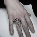 Фото тату: минималистичный черный рисунок на пальце руки, состоящий из абстрактного завитка и точки. Изящный эскиз для любителей лаконичных татуировок.
