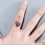 Фото тату: Маленькое изображение сердца, обнимаемого рукой, на безымянном пальце. Минималистичный дизайн, черные линии.