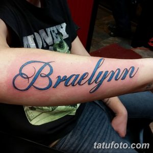 Фото тату: имя 'Braelynn' написано ярким, объемным шрифтом с голубыми и фиолетовыми контурами на предплечье.