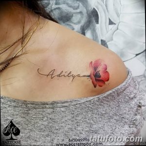 Фото тату: красная акварельная татуировка цветка лотоса и надпись "Aditya" на ключице. Красивый и женственный рисунок татуировки.