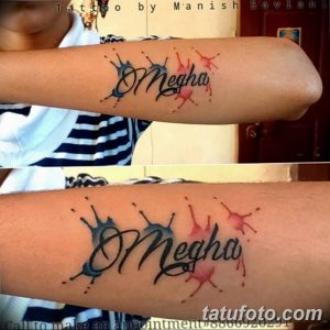 Фото тату надписи 'Megha' на запястье, украшенной брызгами краски. Рисунок татуировки выполнен в ярких цветах, создавая динамичный и креативный образ.