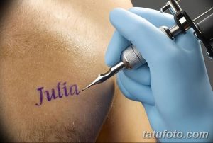 Фотография процесса нанесения татуировки с именем 'Julia', сделанная крупным планом, показывающая руку мастера и тату-машинку.