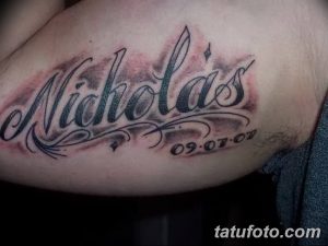 Фото мужской татуировки с именем 'Nicholas' в каллиграфическом стиле и датой '09.07.07', выполненной черными чернилами на плече.