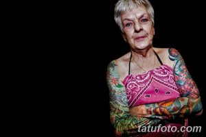 Фото тату: пожилая женщина с яркими, красочными татуировками на обеих руках, с изображением бабочек, цветов и узоров.
