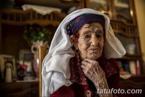 Фото пожилой женщины с морщинистым лицом и татуировками на руках, демонстрирующее ее жизненный опыт и индивидуальность.