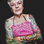 Фото тату пожилой женщины с яркими цветочными татуировками на руках и груди, покрытыми красочными рисунками.