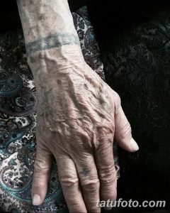 Фото минималистичной татуировки на запястье пожилого человека. Татуировка представляет собой тонкую серую полосу.