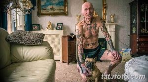 Фото пожилого мужчины с татуировками на теле, позирующего с французским бульдогом. На теле мужчины видны различные рисунки татуировок.