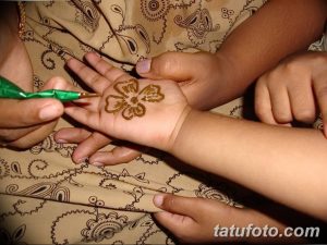 Фото процесса нанесения татуировки хной на руку. Мастер тату аккуратно наносит рисунок с помощью специального инструмента.