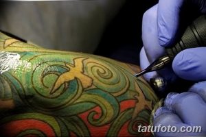 Фото процесса нанесения татуировки на руку: мастер работает над ярким рисунком с использованием разноцветных чернил.