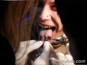 Фото процесса нанесения татуировки на язык. Мастер тату в перчатках работает над рисунком. Крупный план, демонстрирующий детали работы.