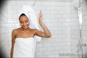 Фотография девушки, выходящей из душа, с полотенцем на голове и улыбкой на лице. Идеально для иллюстрации утренних ритуалов.
