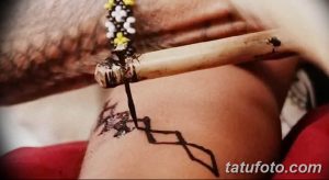 Фотография процесса нанесения татуировки традиционным способом с использованием деревянного инструмента и чернил. Изображение демонстрирует ручную технику татуировки.