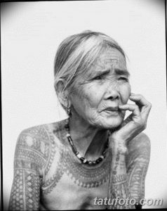 Фотография пожилой женщины с традиционными татуировками на лице и теле. Рисунок выполнен в этническом стиле.