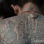 Фото тату: спина мужчины, полностью покрытая сложными татуировками с изображением символов, иероглифов и религиозных мотивов.