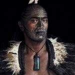 Фотография мужчины с маорийской татуировкой на лице. Видны сложные спиральные узоры, покрывающие его подбородок и щеки.