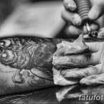 Фотография процесса нанесения татуировки. Виден мастер, работающий над рисунком на руке клиента, используя тату-машинку.