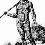 Фотография древнего воина, покрытого сложными татуировками. Видны ритуальные узоры на теле и лице.