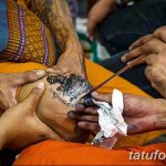 Фотография процесса нанесения татуировки в Таиланде. Виден мастер, использующий бамбуковые иглы для нанесения рисунка на кожу.