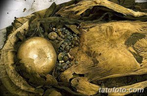 Фотография древнего мумифицированного тела, покрытого татуировками. Видны останки скелета и украшения, свидетельствующие о древних ритуалах.