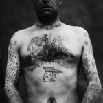 Фото тату: мужчина с обширными татуировками на груди, руках и шее. Рисунки выполнены в стиле олд скул и традиционных морских татуировок.
