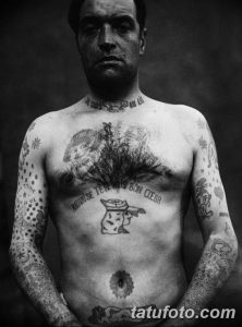 Фото тату: мужчина с обширными татуировками на груди, руках и шее. Рисунки выполнены в стиле олд скул и традиционных морских татуировок.