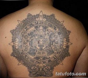 Фотография татуировки календаря ацтеков на спине мужчины. Татуировка выполнена в черном цвете и имеет сложную геометрическую структуру.