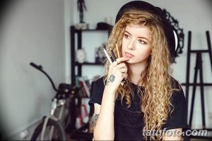 Фото: девушка-тату-мастер с волнистыми волосами, держащая карандаши, задумчивый взгляд, творческая атмосфера.