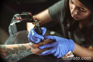 Фото: рука мастера в перчатках, наносящая татуировку с яркими красками, рука клиента с уже нанесенным рисунком.