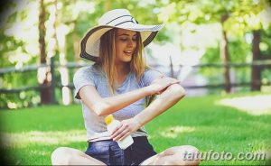 Фото девушки, наносящей солнцезащитный крем на татуировку на руке. Подчеркивается важность защиты татуировки от солнечных лучей.