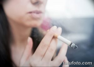 Фото девушки, курящей сигарету. На ее руке видна татуировка, но она не является основным фокусом изображения.